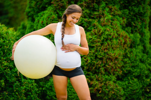 Smiling Pregnant Female Touching Belly While Holding Fitness Ball