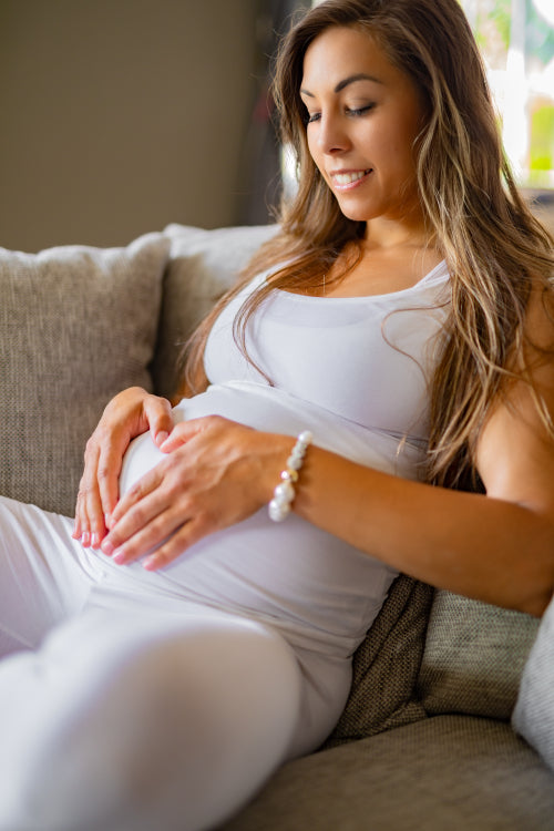 Smiling pregnant woman in sofa forming a heart shape at belly