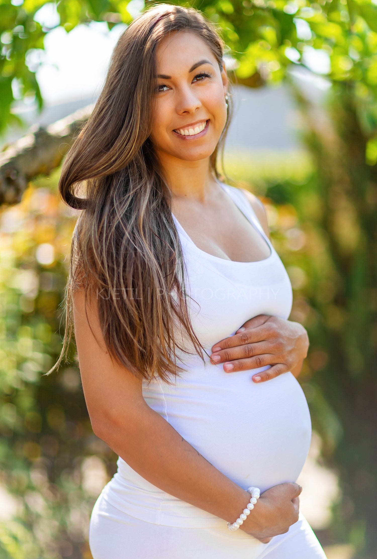 Smiling pregnant woman standing in garden holding hands on belly