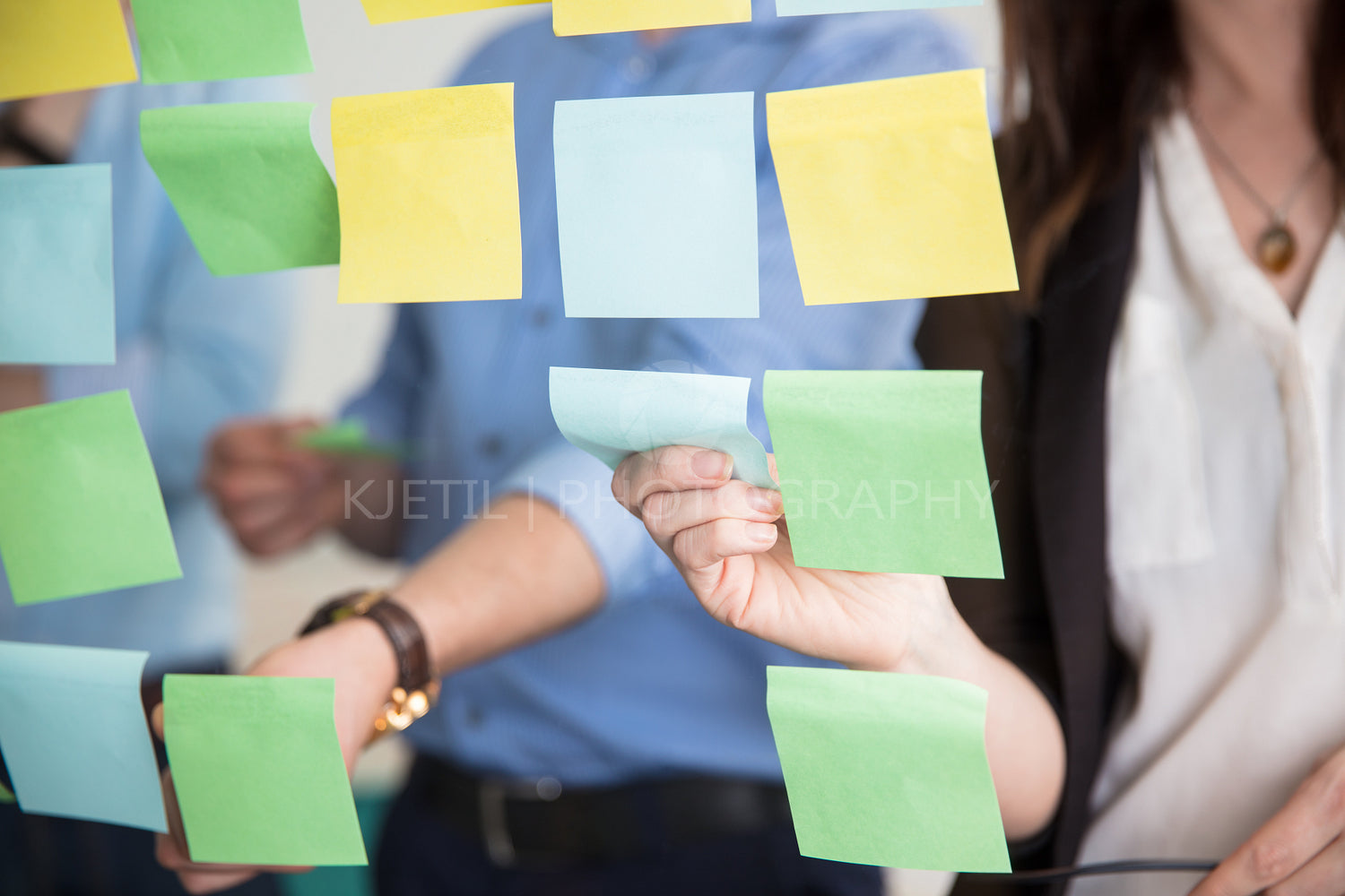 Midsection Of Business People Sticking Adhesive Notes On Glass