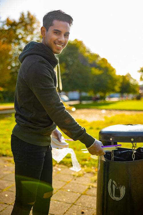 Young man putting straws in garbage bin at park