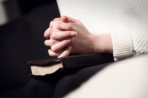 Praying woman folding hands over bible