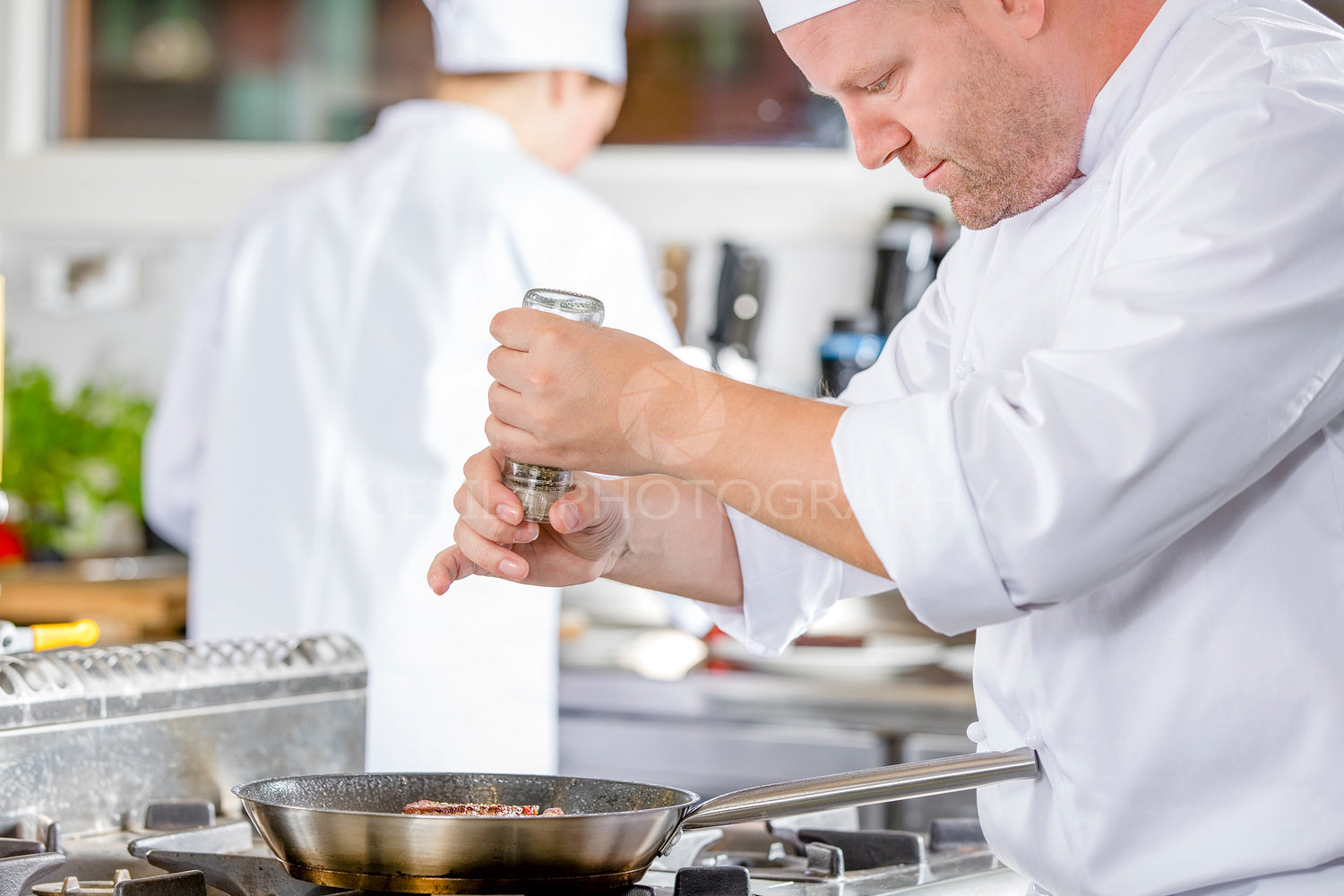 Chef adding pepper on steak in the kitchen