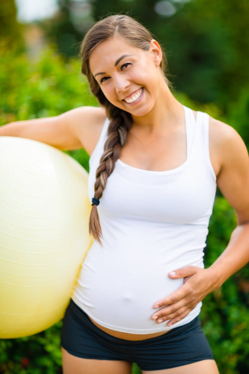 Smiling Pregnant Woman Touching Belly While Holding Exercise Bal