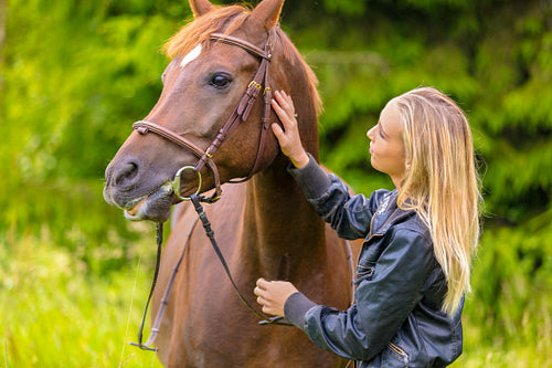 Young woman patting her arabian horse standing in the field