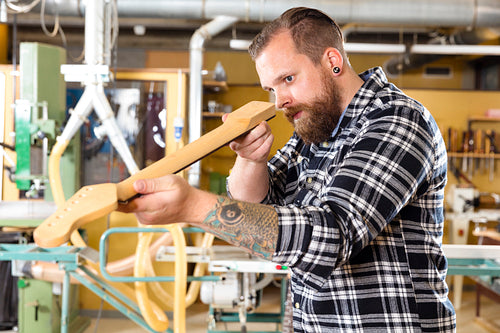 Carpenter inspects a wooden guitar neck in workshop