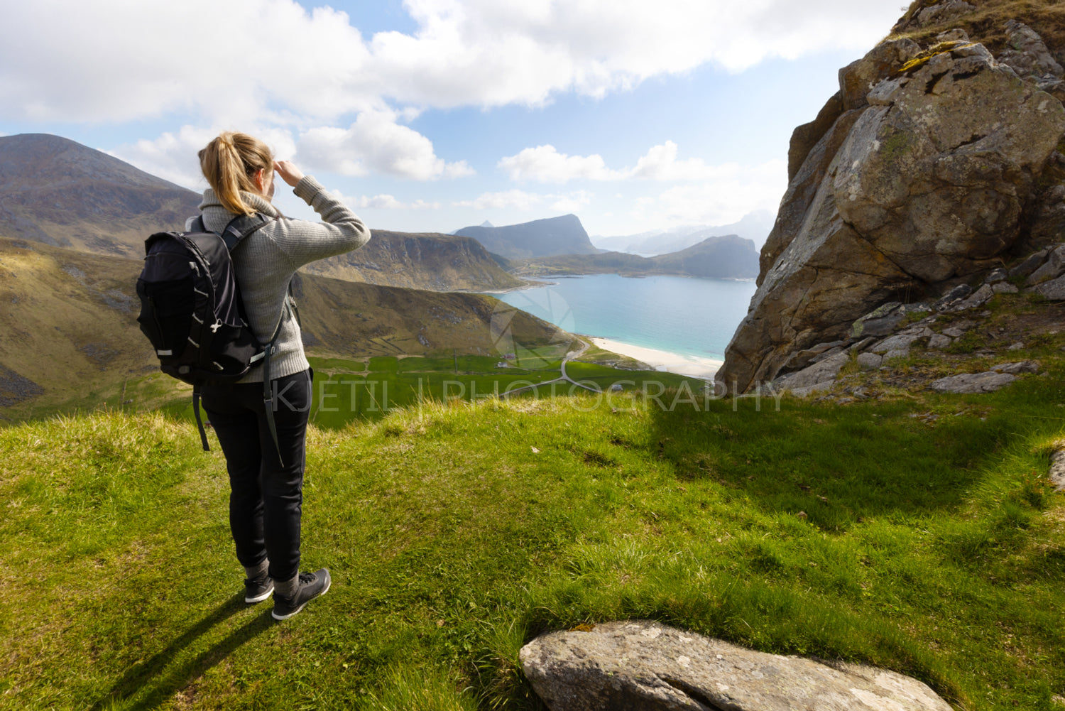 Woman hiking in high mountains and looking at Haukland Beach at Vestvagoy Island at Lofoten, Norway