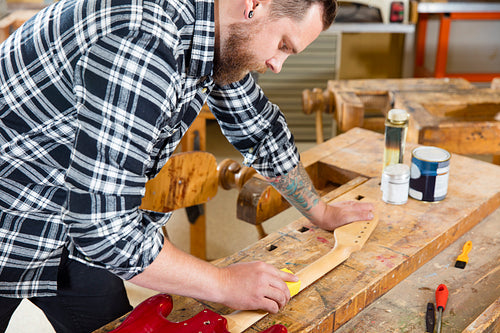 Craftsman sanding guitar neck in wood at workshop