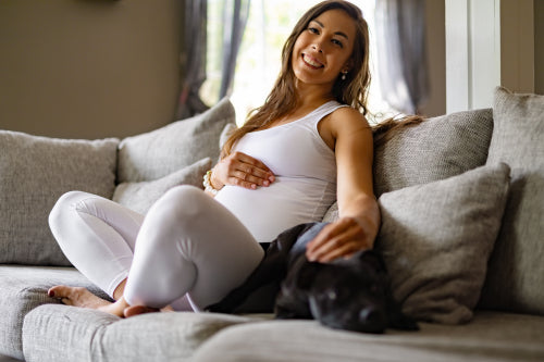 Happy pregnant woman sitting in sofa and pet her dog
