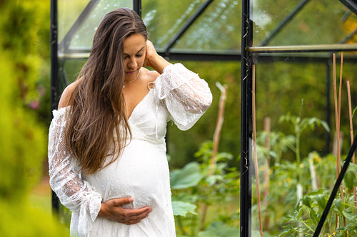 Happy pregnant woman outdoor in her garden looking down on belly
