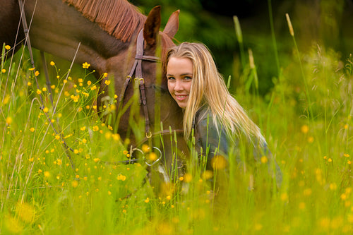Smiling blonde woman sitting in the meadow with her arabian horse