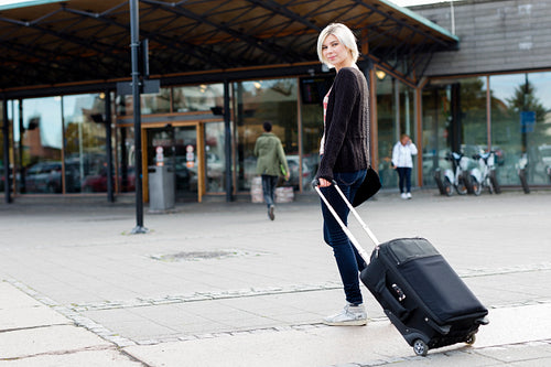 Smiling young woman traveling with a wheeled suitcase