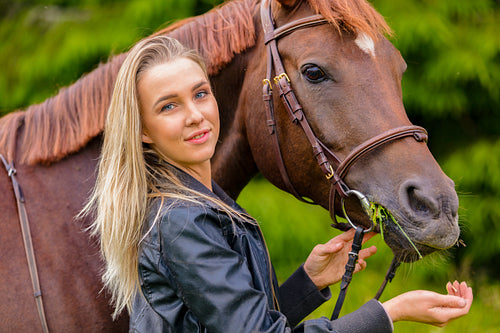 Portrait of a beautiful woman feeding her arabian horse with snacks in the field