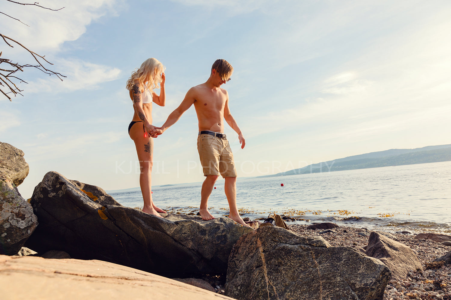 Man Holding Hand Helping Girlfriend On Rocks At Beach