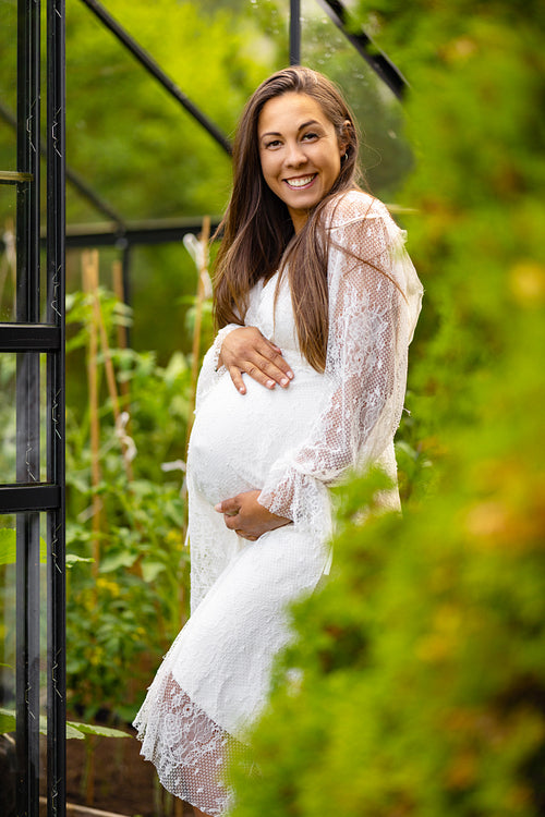 Smiling pregnant woman outdoor in her garden holding hands on belly
