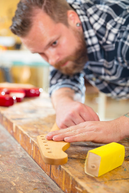Carpenter sanding a guitar neck in wood at workshop
