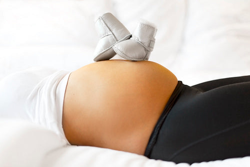 Pregnant woman in bed with baby shoes on her belly