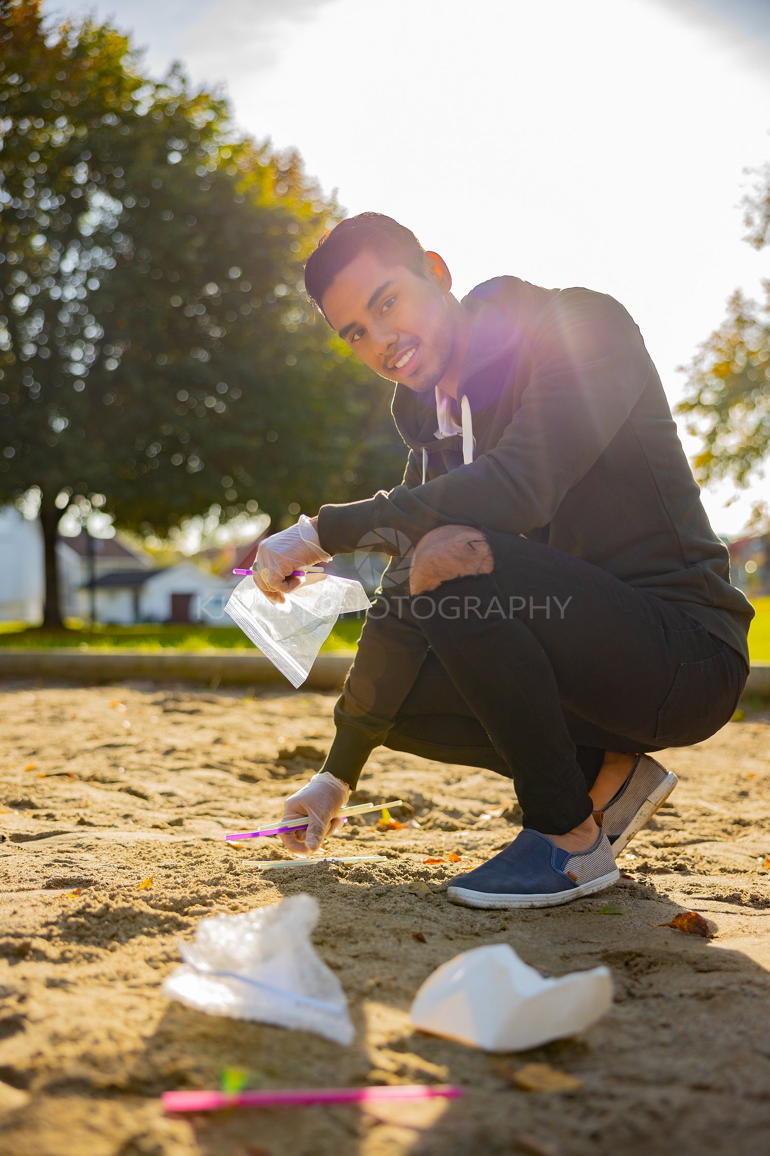 Back lit of smiling man cleaning garbage on sand at park