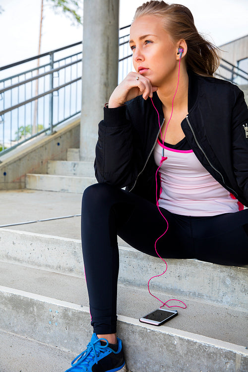 Thoughtful Sporty Woman Listening Music While Sitting On Steps