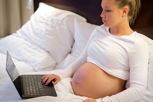 Pregnant woman in her bed working on computer