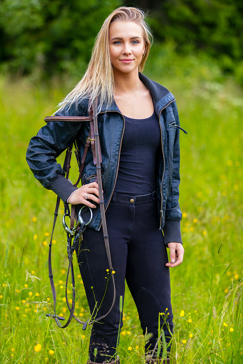 Beautilful young female horse rider standing in a green meadow