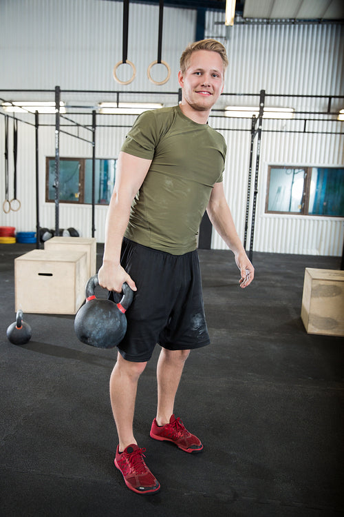 Confident Male Athlete Lifting Kettlebell In Health Club