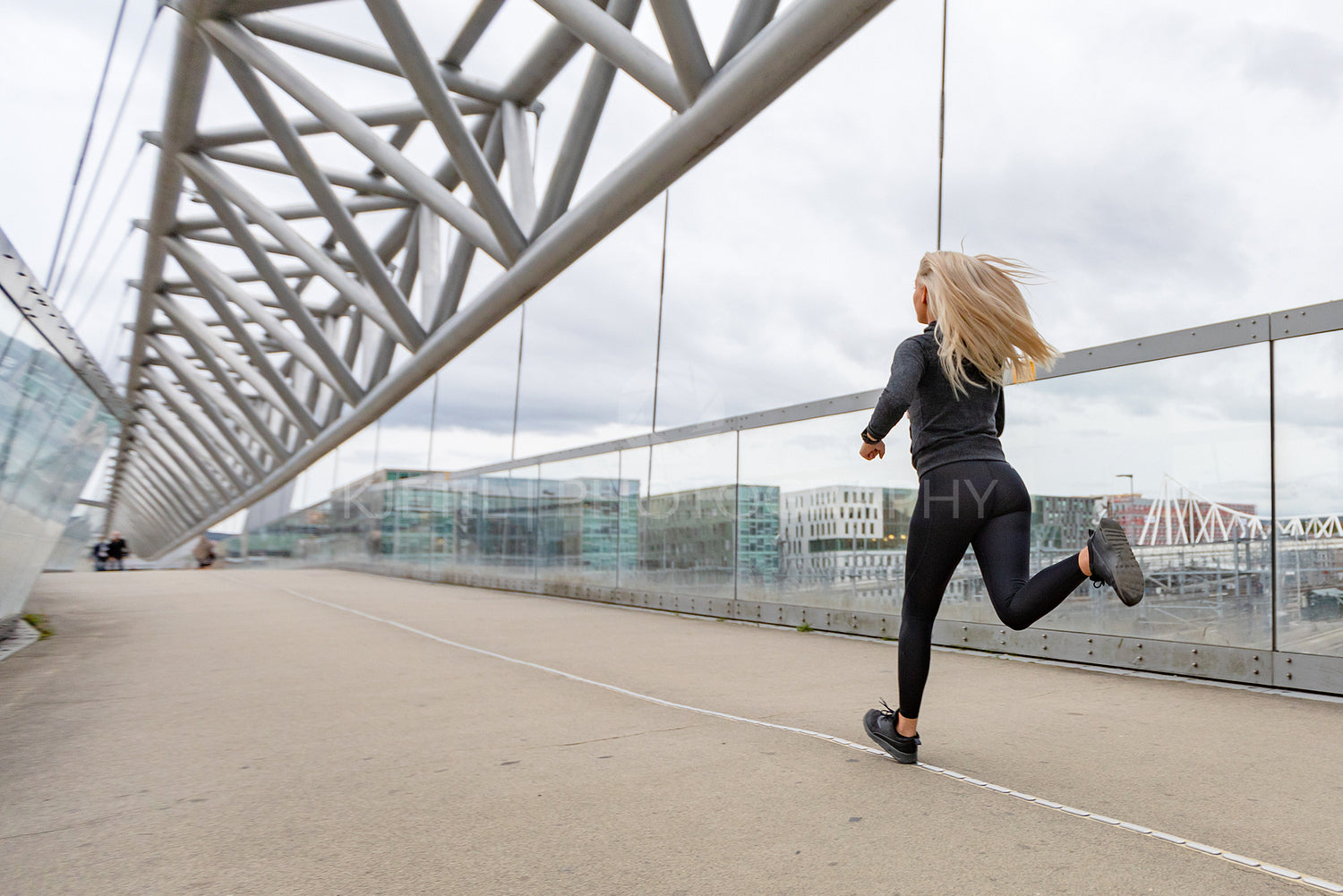 Blonde woman runner in black workout outfit in modern city environment