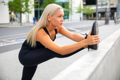 Confident Female Athlete Stretching Leg On Railing At Sidewalk