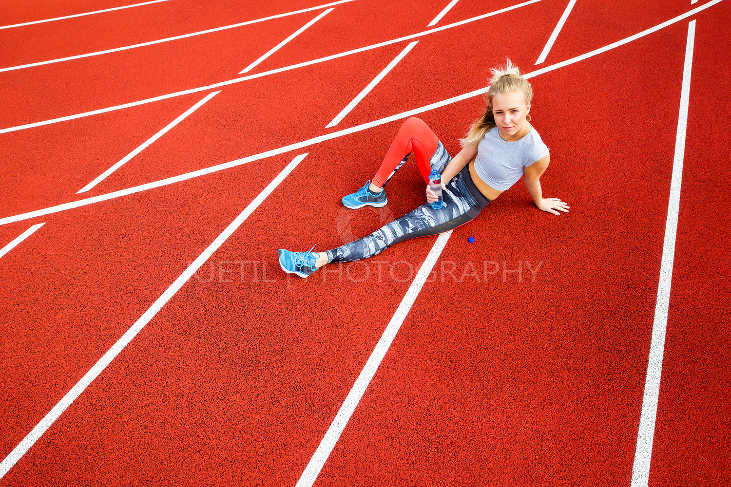 Sporty Woman With Water Bottle Sitting On Running Tracks