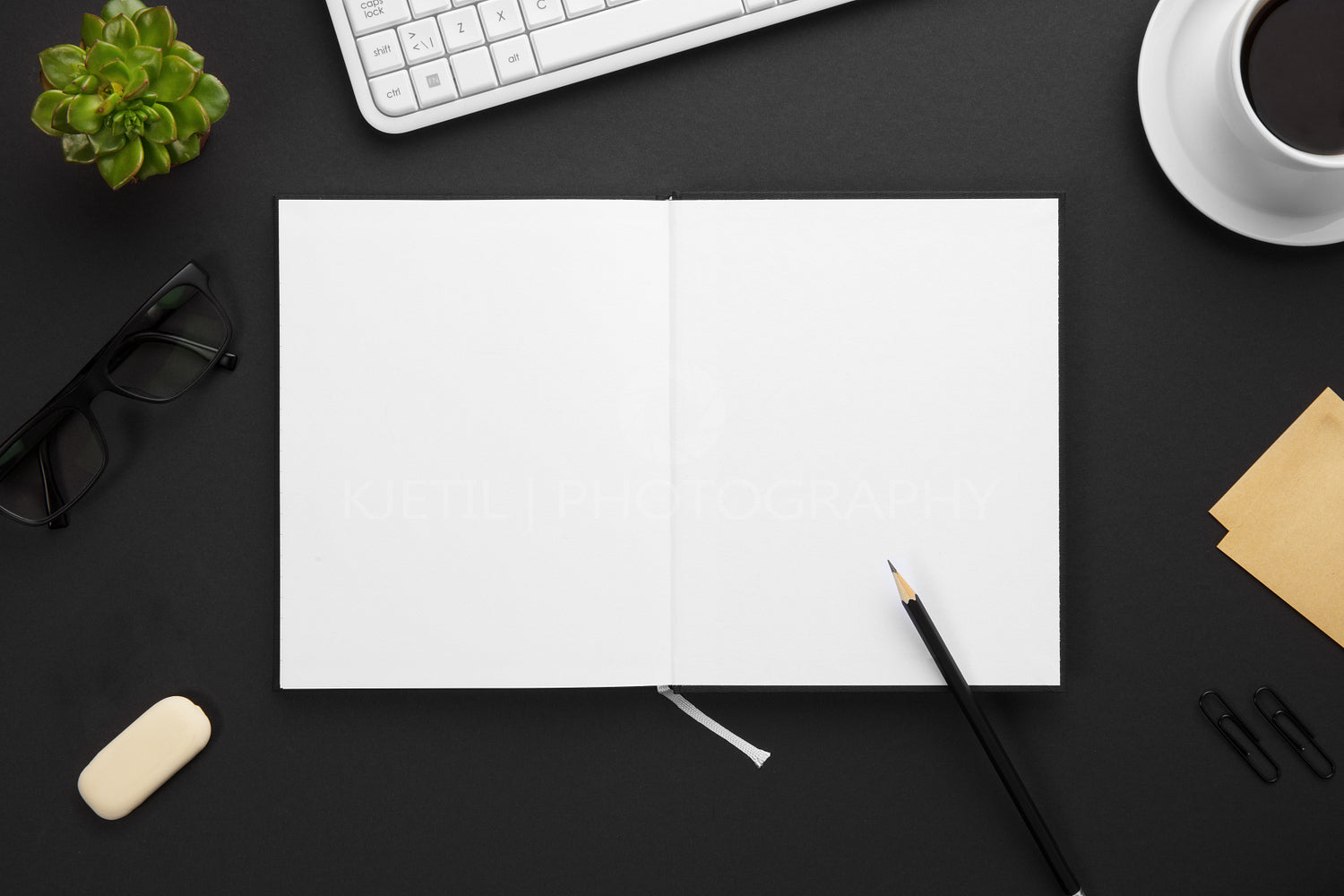 Top View of Blank Paper in Note Book Surrounded By Office Supplies On Gray Desk