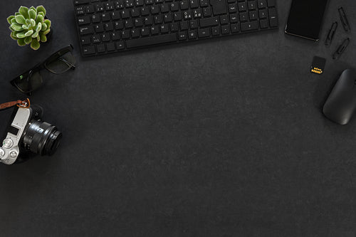 Top view of black concrete office desk with computer, camera and supplies