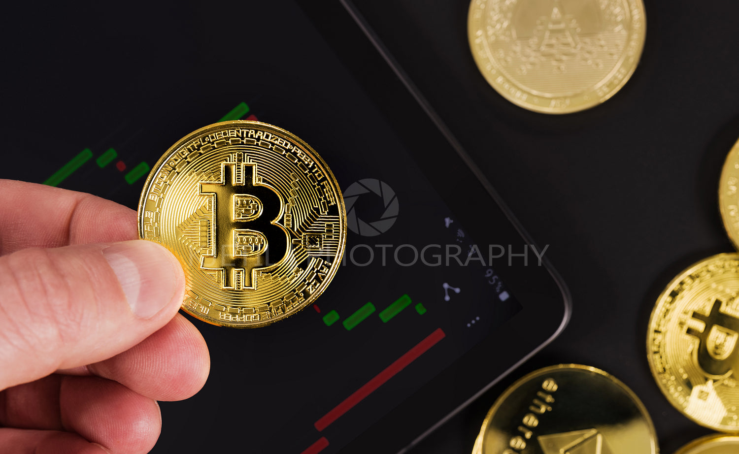 Hand holding Bitcoin over digital tablet by coins
