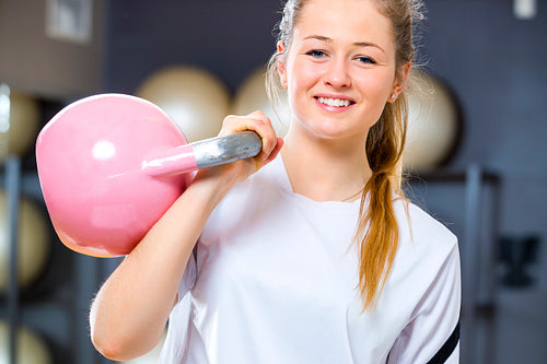 Young cheerful woman holds kettlebell at fitness gym center
