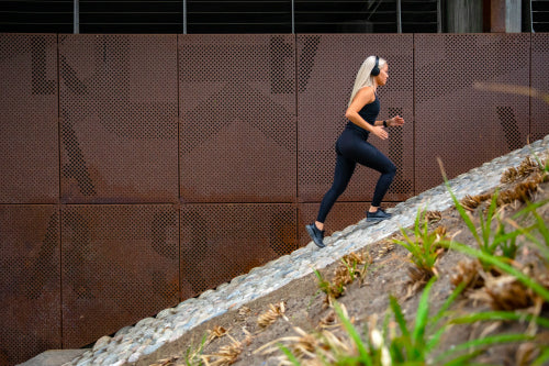 Fit sports women running interval workout in stairs against a metal wall in city