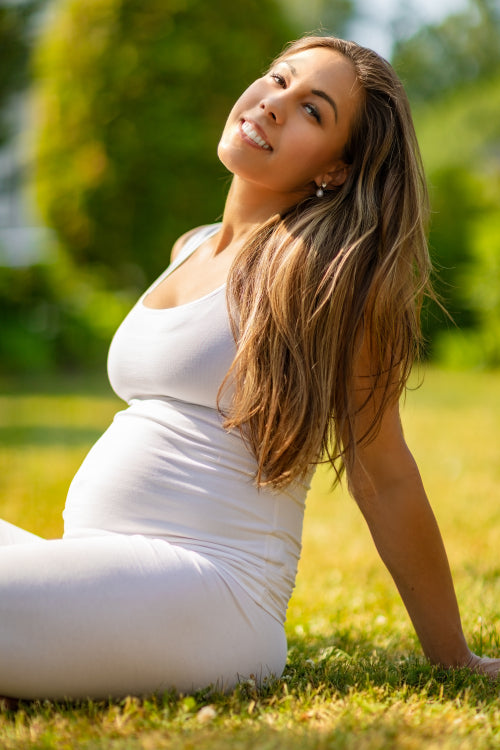 Cheerful pregnant woman sitting on the grass in a beautiful garden