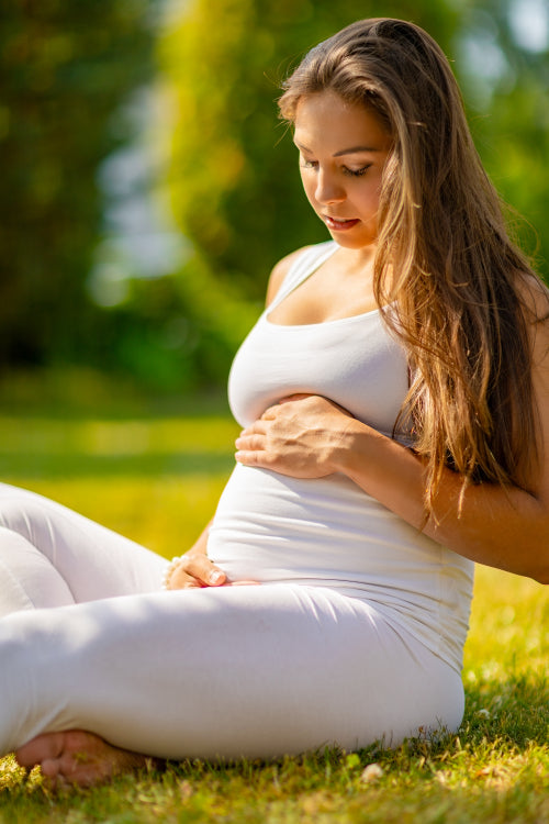 Happy pregnant woman sitting on the grass in a beautiful garden