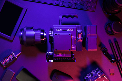 Overhead view of cinema camera and computer parts on colorful illuminated table
