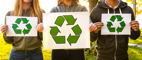 Wide view of team of environmental protection volunteers holding recycling symbol placards
