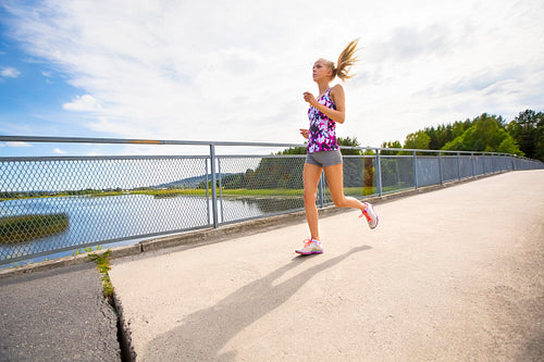 Motivated young woman running fast on bridge over a lake