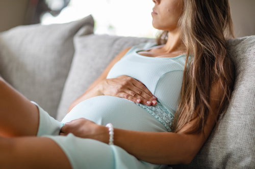 Mid-section of worried pregnant woman in sofa with her hands at belly
