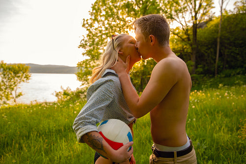Young Shirtless Man Kissing Girlfriend During Sunset In Idyllic Nature