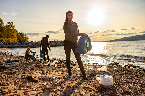 Woman cleaning beach with volunteers during sunset