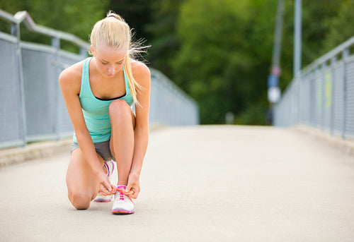 Young woman runner tying shoelaces on bridge