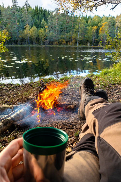Man relaxing ourdoor by the fire in the forest with a coffee