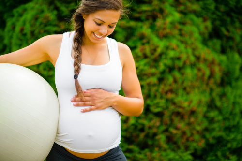Pregnant Woman Touching Abdomen While Holding Fitness Ball In Park