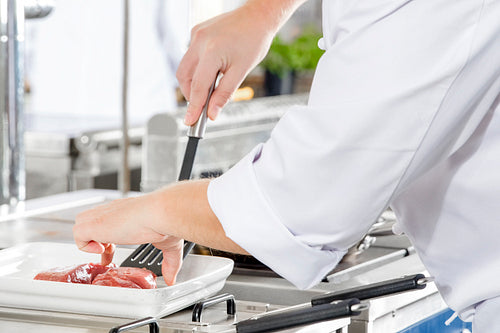 Close-up of a chef prepares beef steak in pan at the kitchen