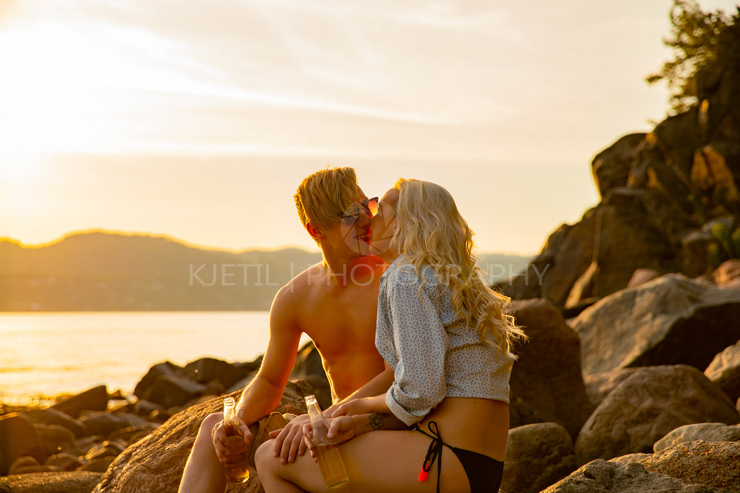 Close-up of Romantic Couple Kissing And Drinking Beer While Sitting On Rocks