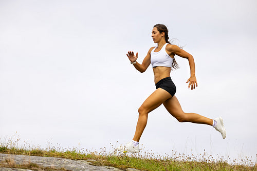 Determined Fit Female Athlete Running On Mountain Against Sky