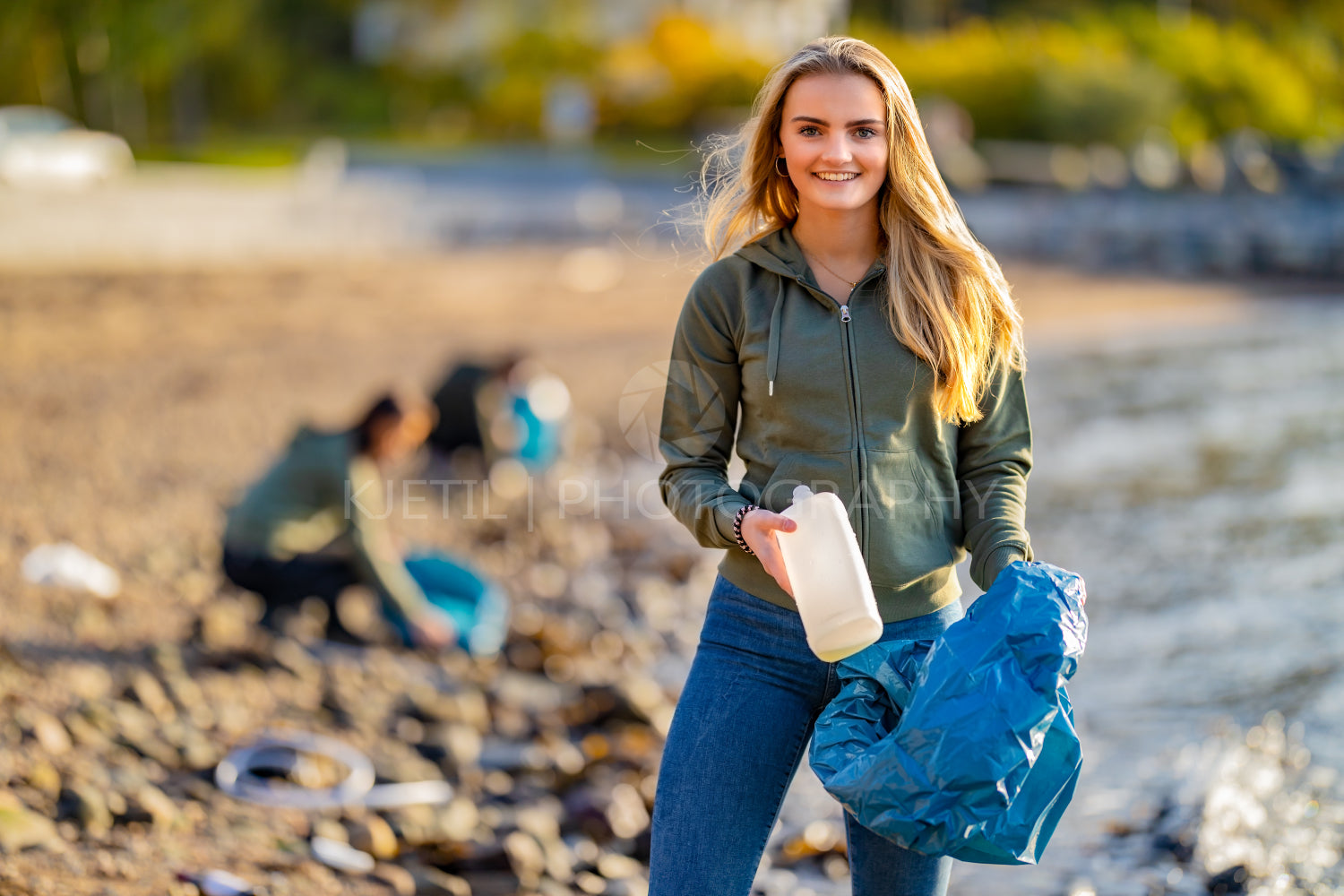 Smiling volunteer holding bottle and garbage bag at beach