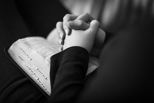 Praying and Folding Hands over a Bible